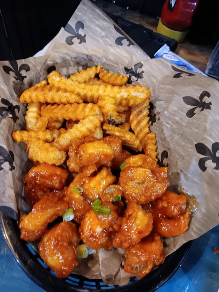 Sauced chicken wings and crinkle fries in a basket lined with fleur-de-lis paper